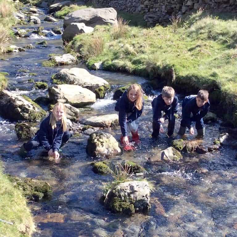 students in a river in wellies