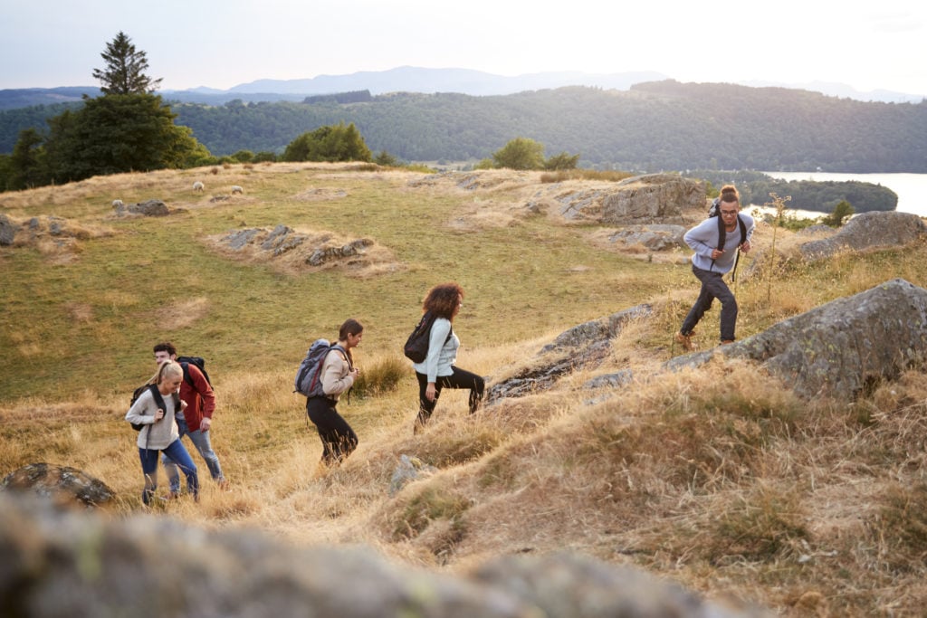 A multi ethnic group  of five young adult friends smile while climbing to the summit during a mountain hike, side view