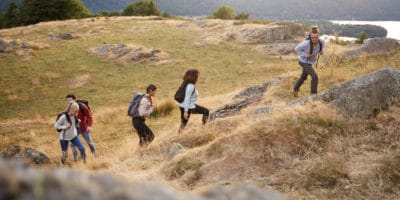 A multi ethnic group of five young adult friends smile while climbing to the summit during a mountain hike, side view