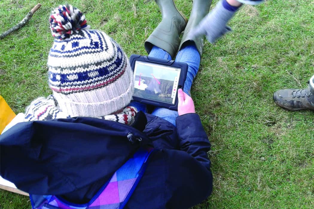 Girl using ipad wearing welllies and woolly hat