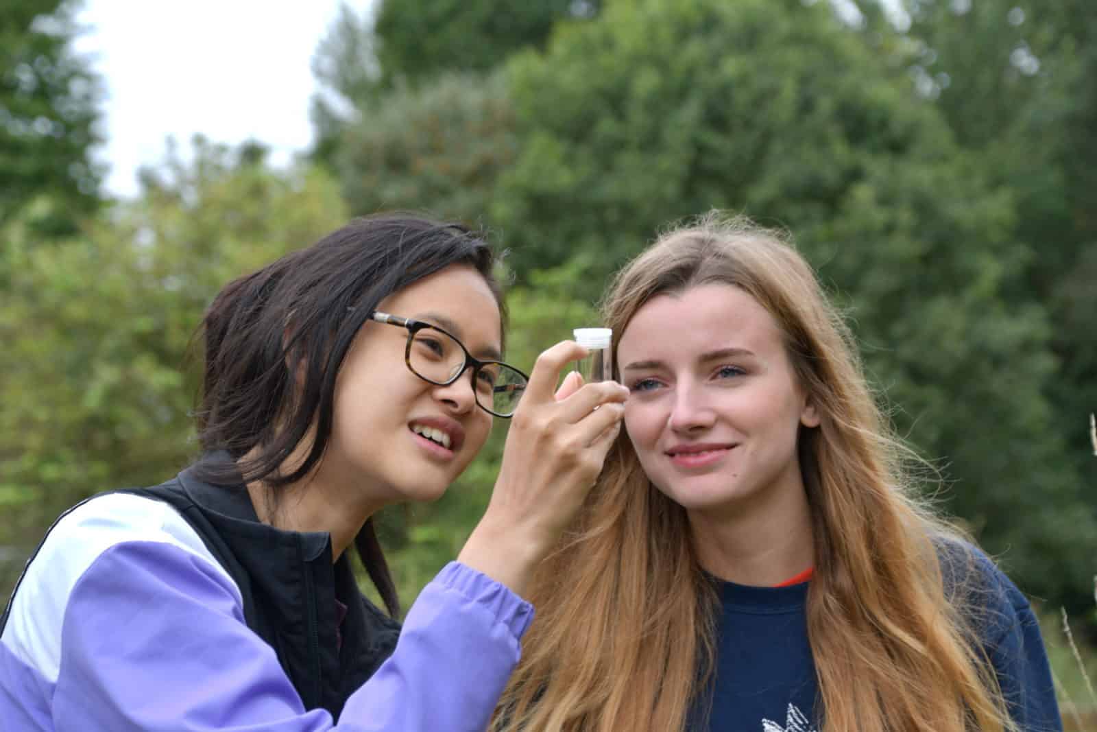 Two girls looking at insect in identification pot