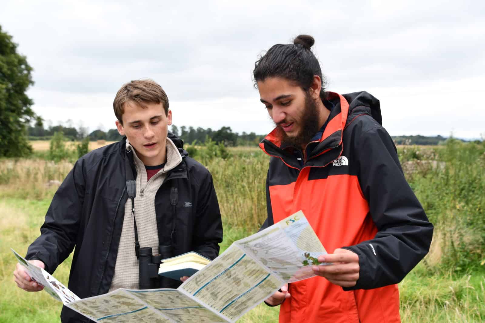 Two young people outdoors looking at wildlife ID guide