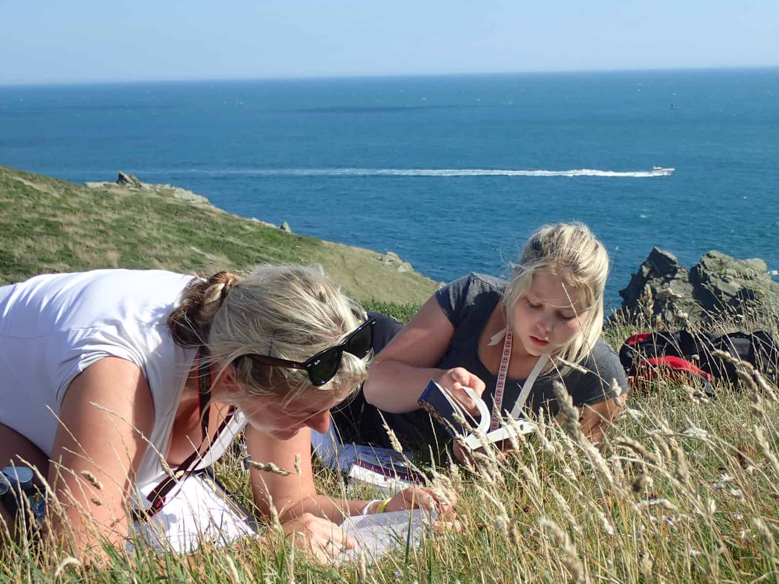 Two ladie looking in the grass with the coast behind them