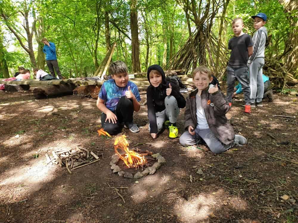 A group of 3 boys achieving to light a camp fire