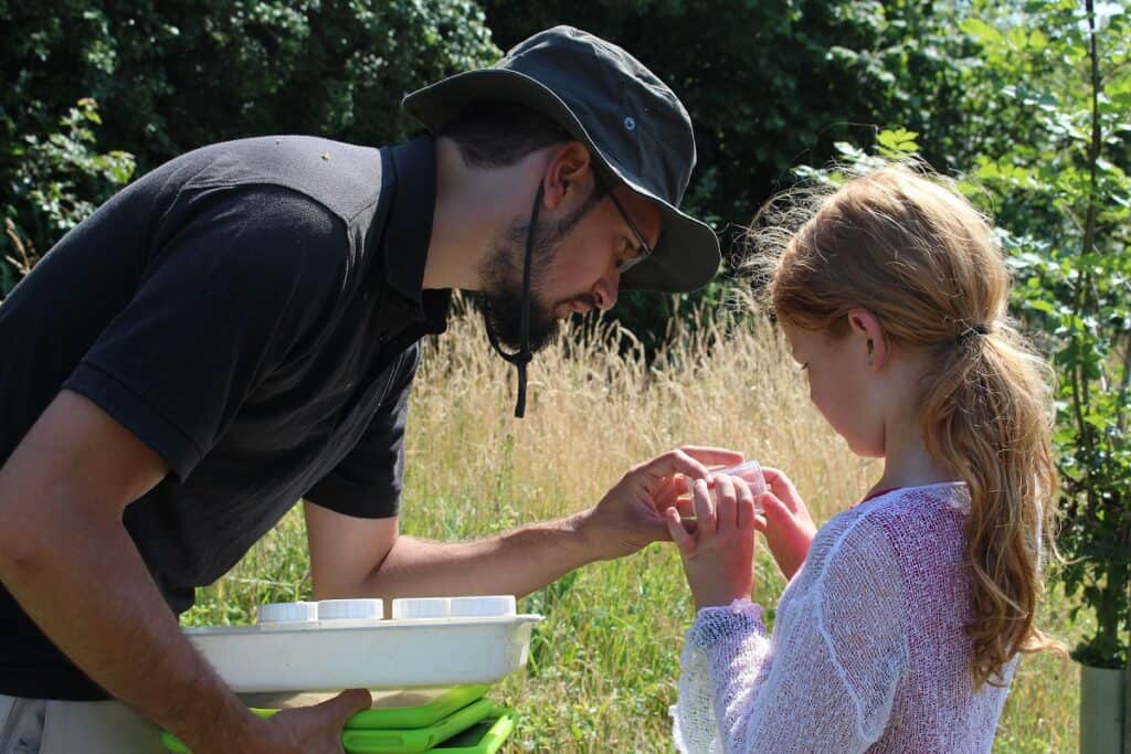 A tutor is showing a young girl something from a bug hunt