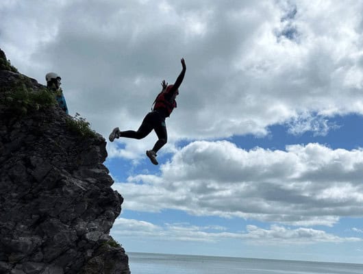 A girl jumping off a rock into the sea
