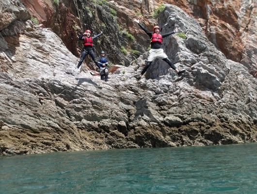 Two people jumping off a rock into the sea
