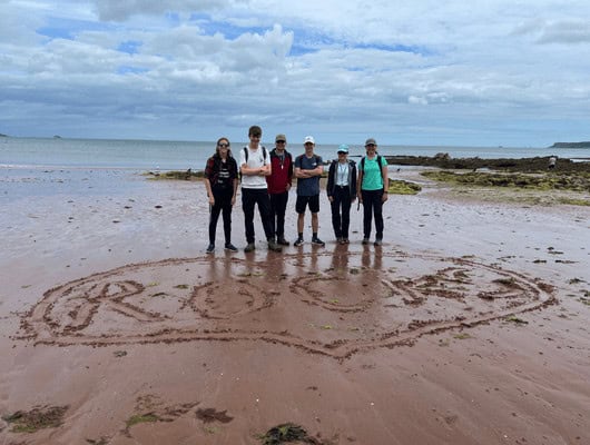 A group of people stood behind some sand art that say 'rocks' in a heart