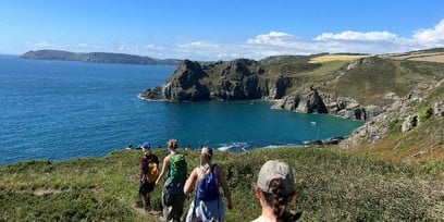 A photograph of a group of people walking along a hill with a view of the sea