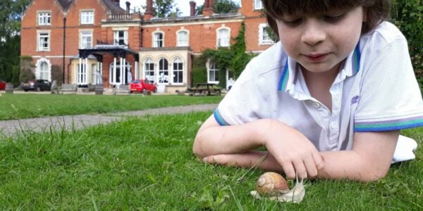 boy looking at a snail with Juniper Hall in the background