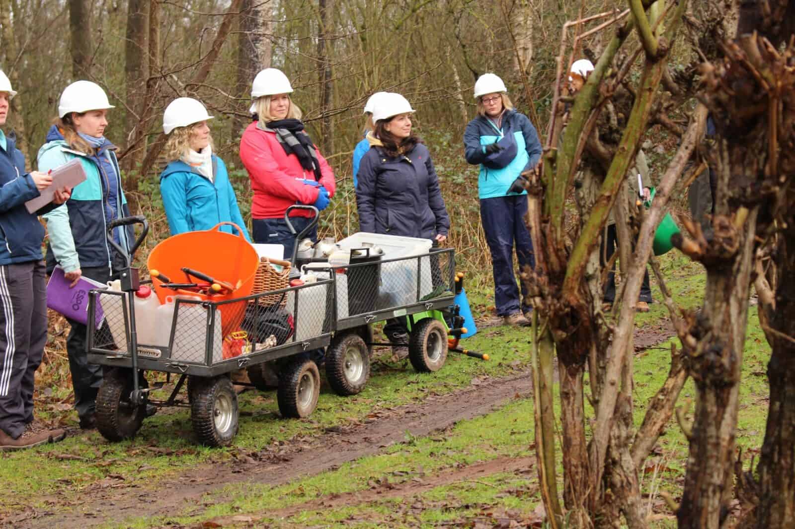 8 people dressed in outdoor clothing and hard hats watching a forest school demonstration