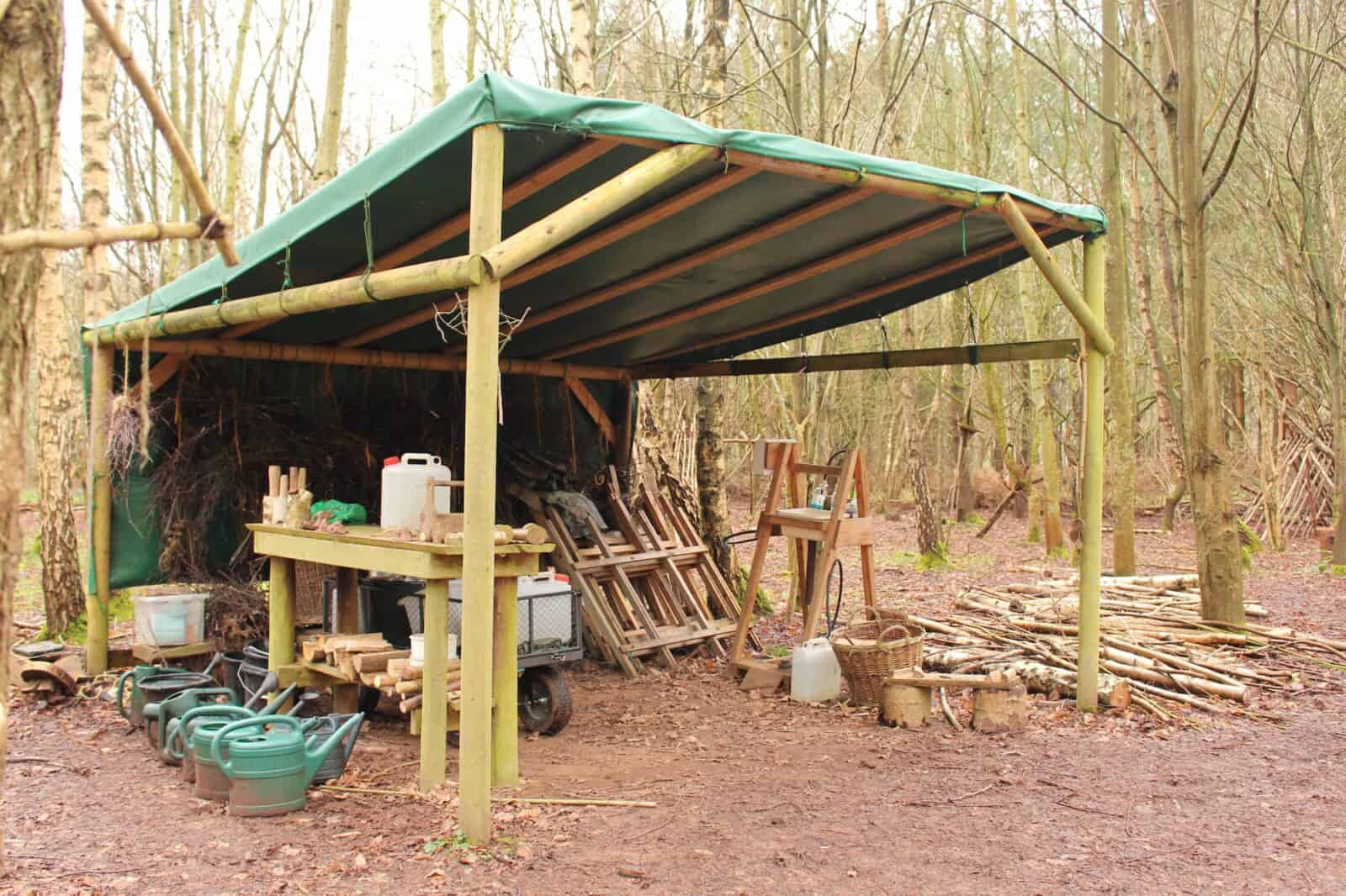 Outdoor classroom structure in a wood with a green canvas roof and contains forest school equipment