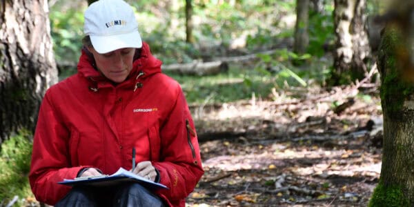 woman in red jacket in the woods taking notes