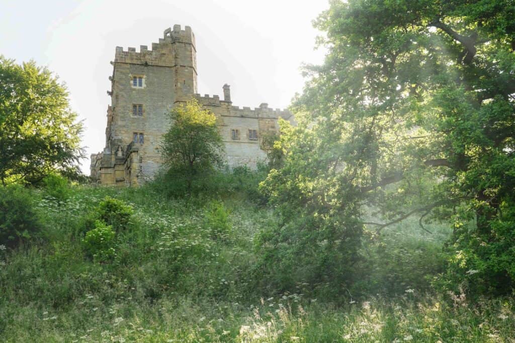 he 12th century manor house that is Haddon Hall, surrounded by greenery.