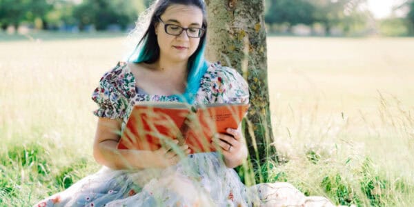 A photograph of a women in a field reading a book