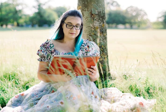A photograph of a women in a field reading a book
