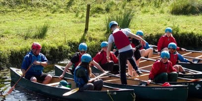 A photograph of a group of teens in canoes