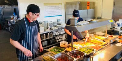 Catering staff serving hot food from behind a hot food counter.