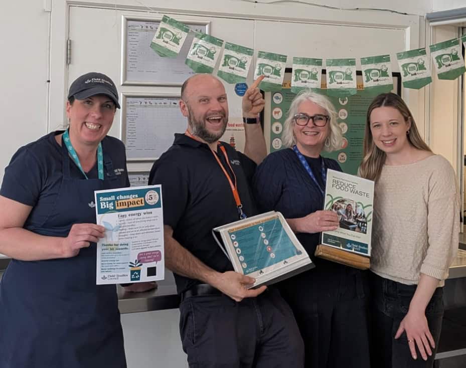 Three women and a man are smiling and holding up food waste posters and certificates.