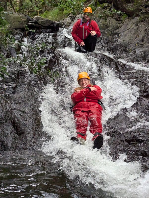 A young person sliding down a river - Adventure+ Camp
