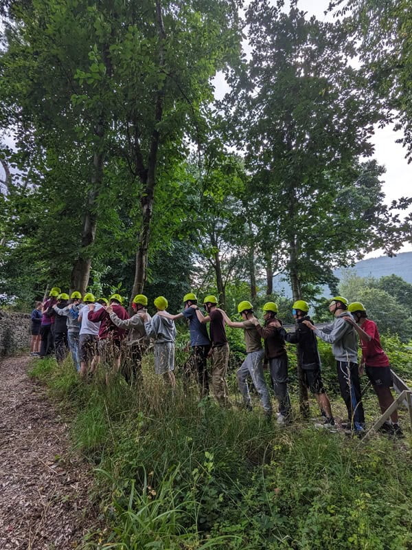 An image of young people, all wearing helmets and walking in a line - Adventure+ Camp