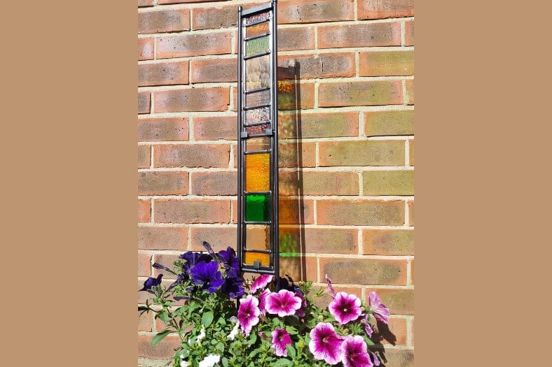 A photo of a stained glass sculpture against a brick wall - stained glass garden art.